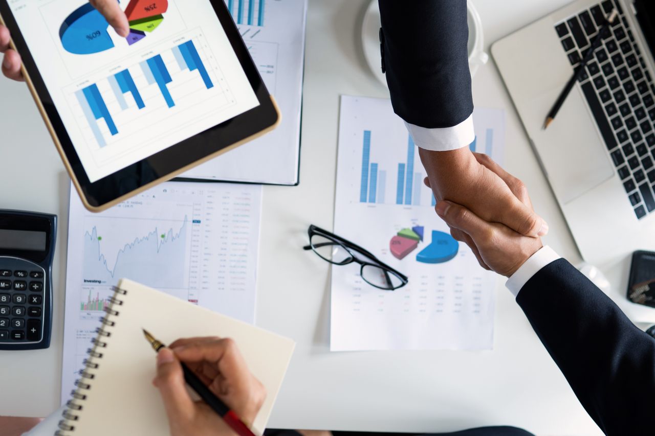 Home Business professionals handshake over graphs and charts in a corporate setting, symbolizing successful negotiation and agreement.